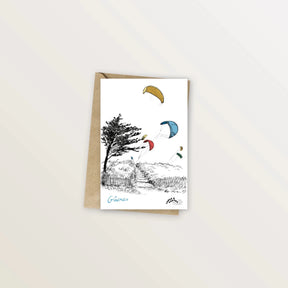 Carte postale Gâvres : kitesurfs colorés au-dessus des dunes et d'un pin tordu par le vent