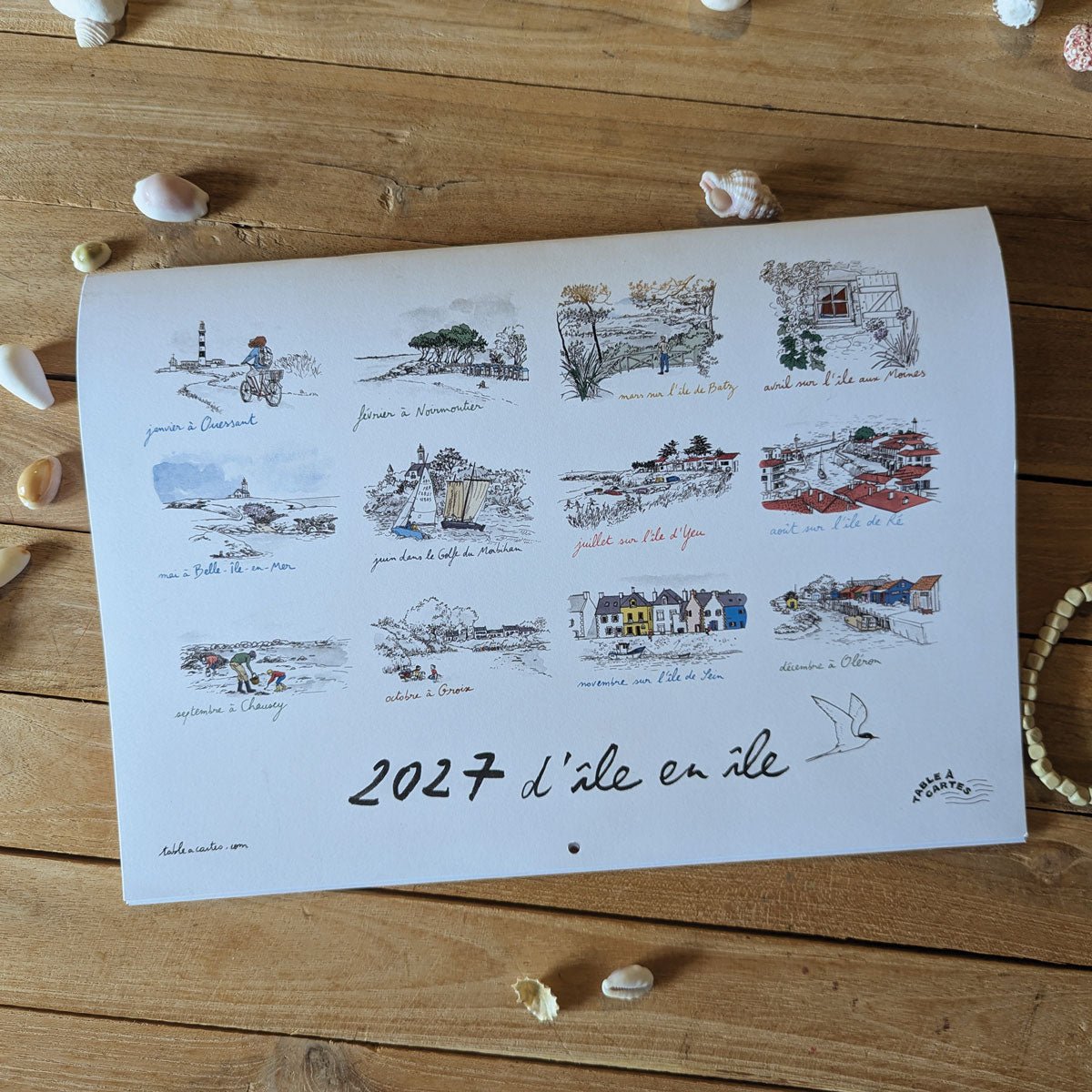 Couverture du calendrier 2027 « D'île en île » posée sur une table parmi des coquillages