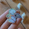 Sticker brillant « 4 coquillages » tenu entre les doigts, reflets holographiques